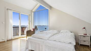 Een slaapkamer met een groot raam, een bed, een nachtkastje en een stoel bij het raam.