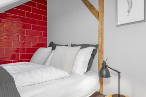 A bedroom with a red brick wall, a white bed, and a black desk lamp.