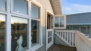 Een houten terras met een witte balustrade, een beeld en een gebouw met grote ramen en een metalen dak.