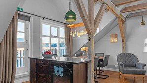 Een keuken met houten balken, een modern kookeiland, en een eethoek met een grijze fauteuil.