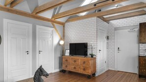 Een kamer met een houten plafond, witte bakstenen muren, een houten dressoir met lades, een televisie erop en een beeldhouwsel van een paard op een tafel.