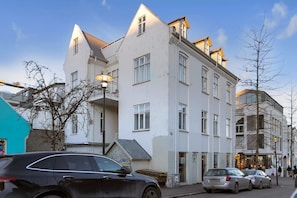 En bygning med flere etager, hvid facade, altaner og udsigt over gaden med parkerede biler.
