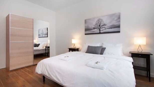 A bedroom with a bed, two bedside tables, a wardrobe, and a wall-mounted painting.