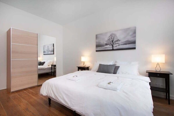Un dormitorio con cama, dos mesitas de noche, un armario y un cuadro colgado en la pared.