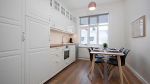A modern kitchen with white cabinets, a dining table with chairs, and a large window.