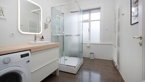 A modern bathroom with a glass shower enclosure, a built-in washing machine, and a large mirror.
