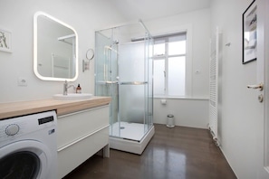 Un baño moderno con cabina de ducha de vidrio, lavadora integrada y un espejo grande.