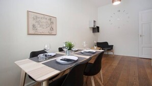A dining area with a long table, chairs, a clock, a framed picture, and a small plant.