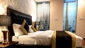 Habitación de hotel con una cama grande, una mesita de noche con lámpara y vistas al exterior a través de cortinas.