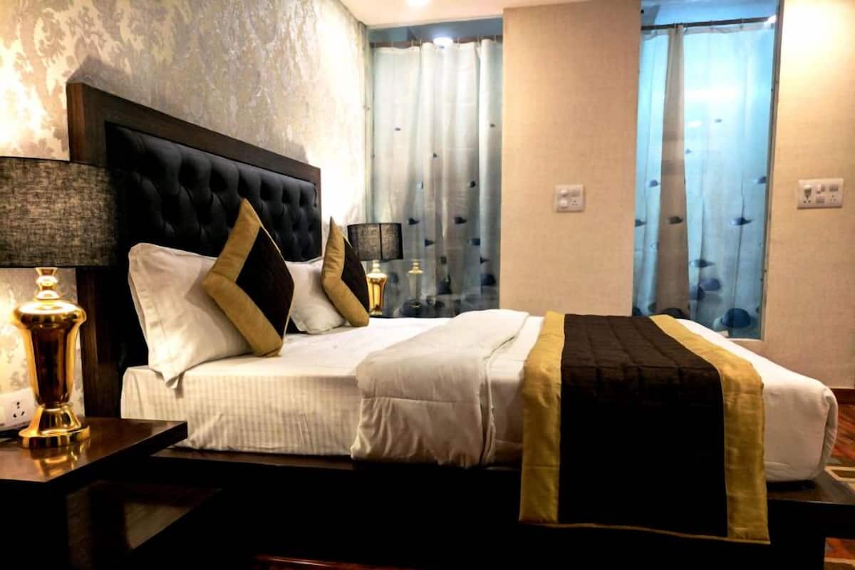 Habitación de hotel con una cama grande, una mesita de noche con lámpara y vistas al exterior a través de cortinas.