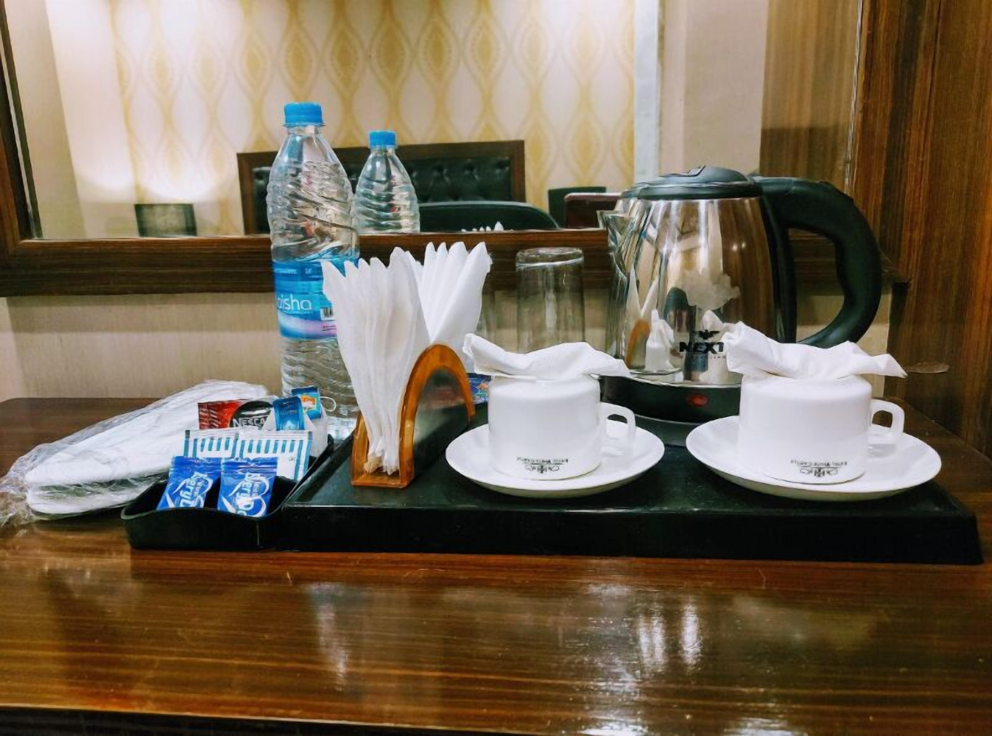 A hotel room's breakfast setup with a tray containing two white cups, a glass pitcher, a bottle of water, and a box of tissues.