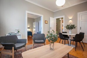 A modern living room with a wooden dining table, two grey armchairs, a small white side table, and a potted plant. - Beautiful apartment in heart of RVK (Reykjavík)