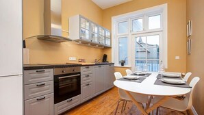 Una cocina moderna con armarios grises, horno empotrado y comedor con mesa y sillas blancas.