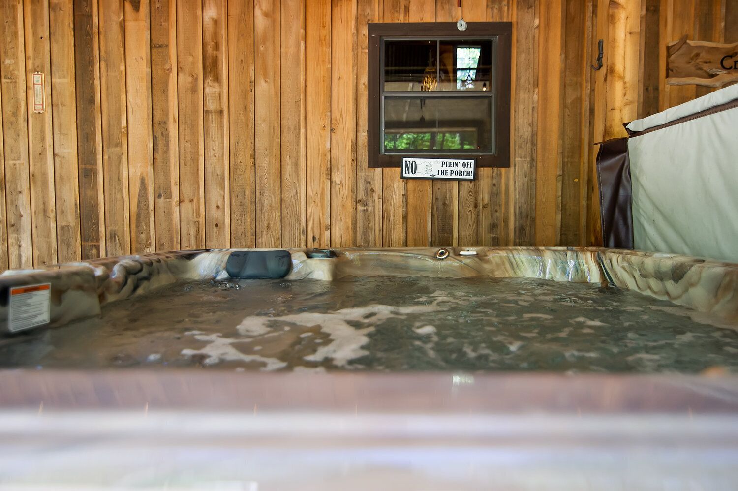 Un intérieur en bois avec un jacuzzi, un panneau indiquant qu’il est interdit d’entrer sur la véranda, et une fenêtre donnant sur la verdure.