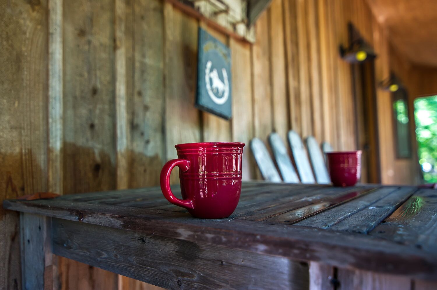 A rustic wooden table with a red mug and a blue sign with a white symbol on the wall behind it.