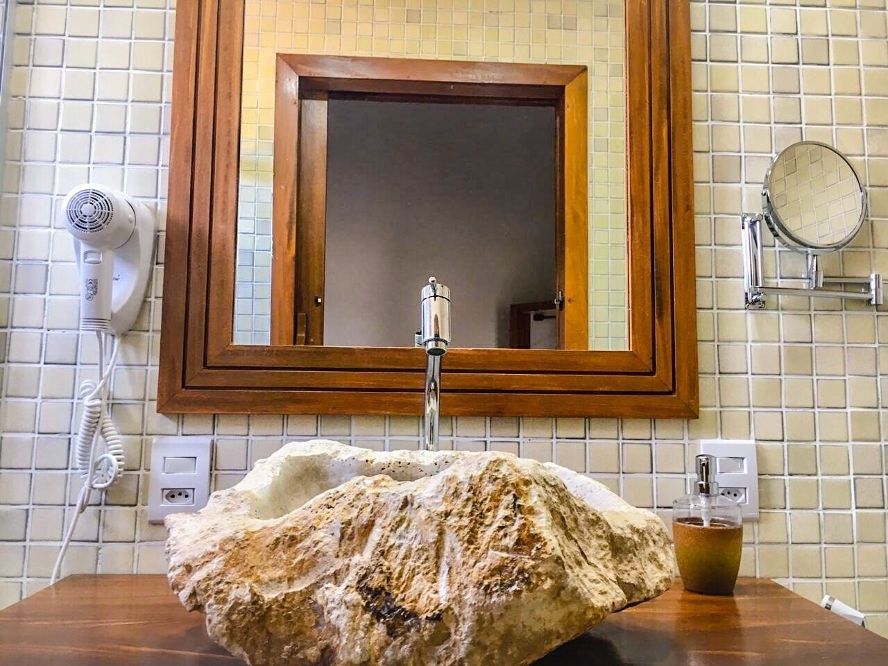 Un baño con un lavabo de piedra grande, un espejo con marco de madera, un secador de pelo y un espejo redondo en la pared.