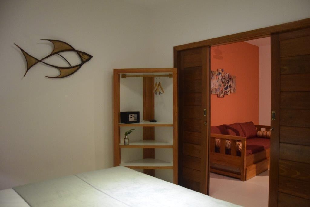 A bedroom with a bed, a wooden wardrobe, a wall-mounted shelf with a radio and a plant, and a fish decoration.