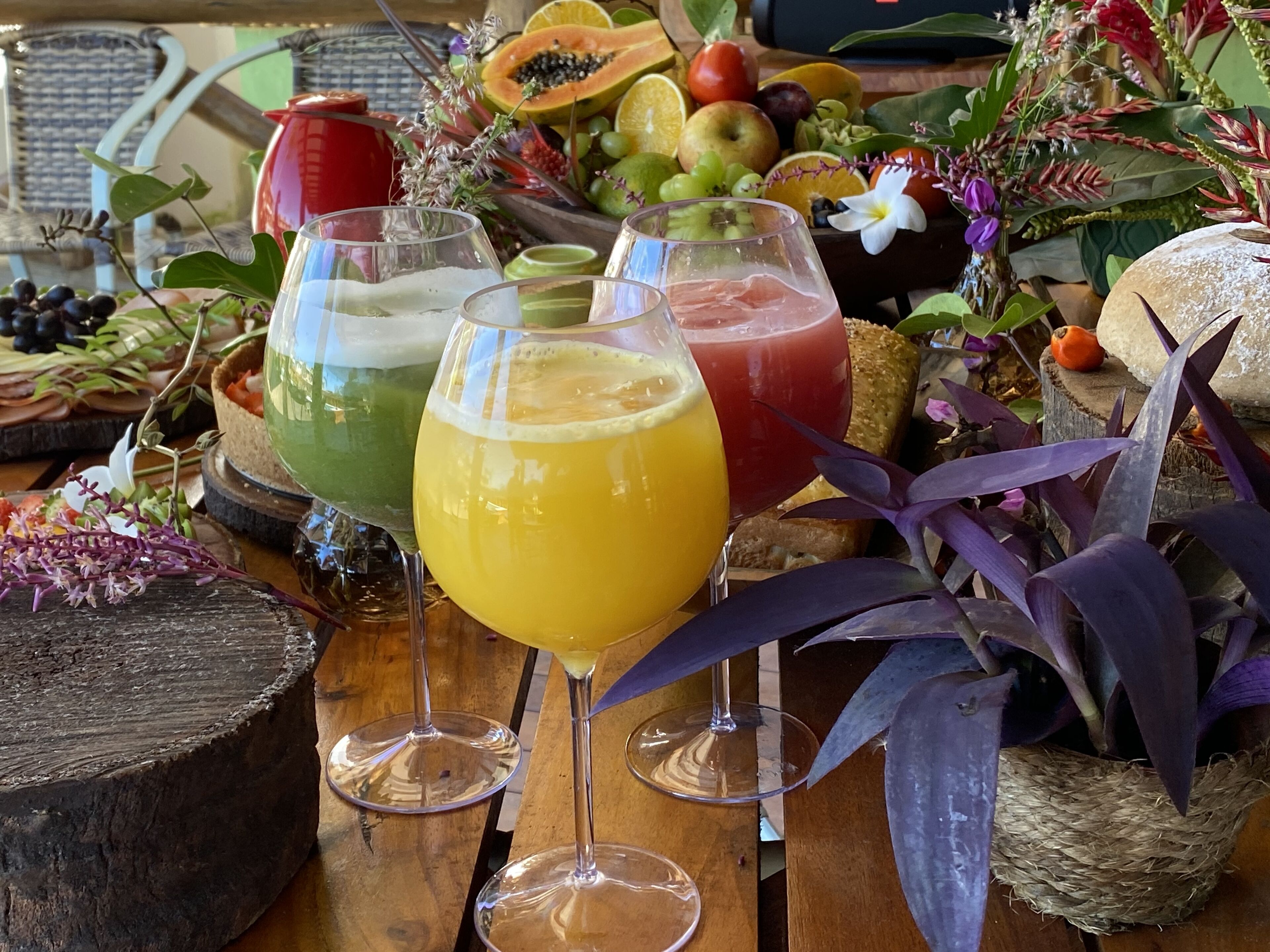 Een tafel met drie glazen sap, een fruitschaal en een decoratieve plantenarrangement.
