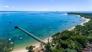 A coastal view with a pier extending into the sea, surrounded by lush greenery and clear blue waters. - Carapitangui Pousada (Maraú)