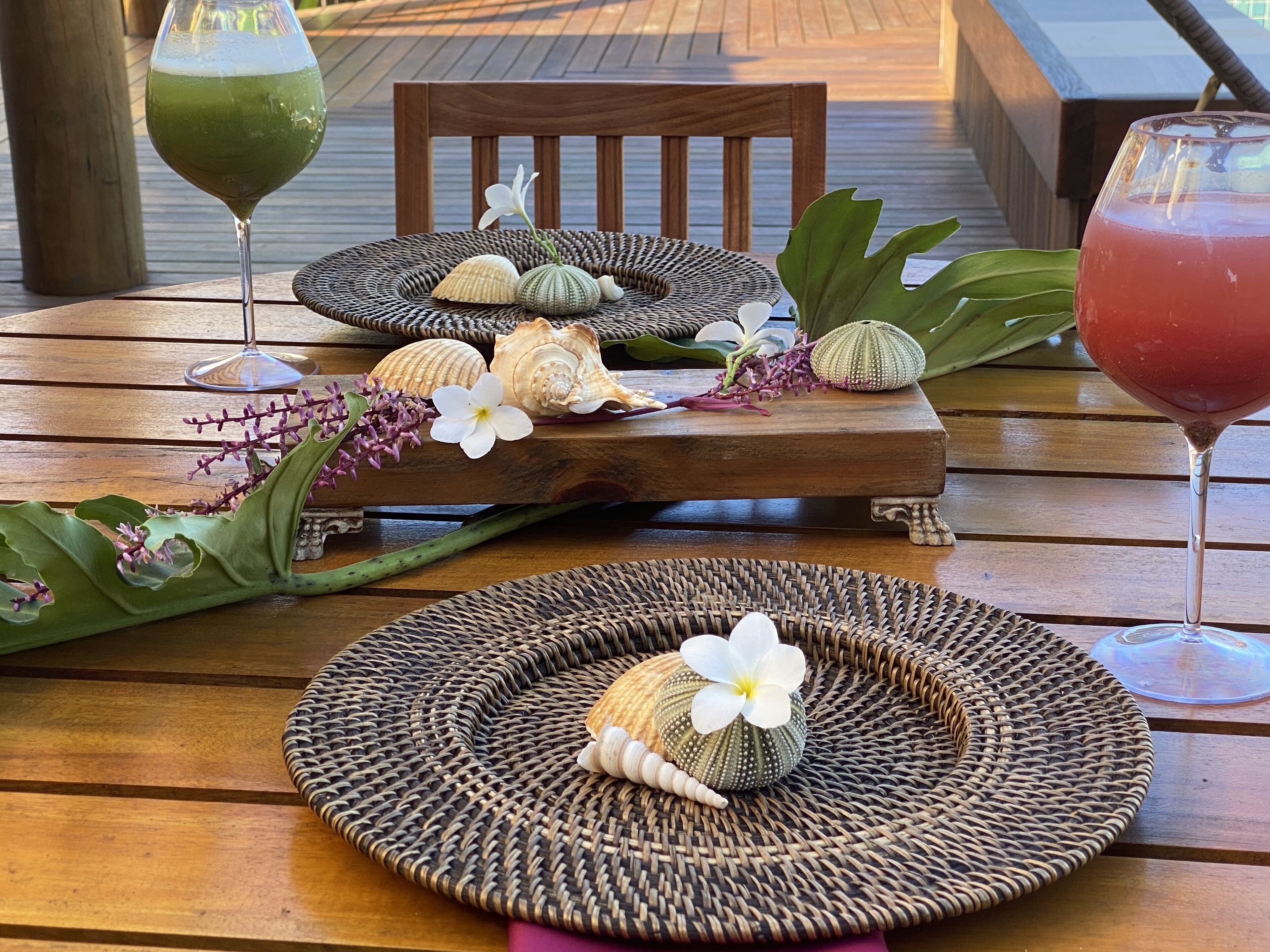 A wooden table with woven placemats, decorative shells, and flowers.