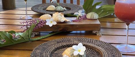 A wooden table with woven placemats, decorative shells, and flowers.
