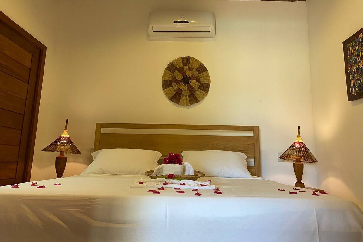 Una cama bien hecha con sábanas blancas, un tapiz decorativo y dos lámparas de noche.