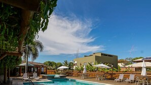A swimming pool with lounge chairs and umbrellas, surrounded by wooden fences and palm trees. - Carapitangui Pousada (Maraú)