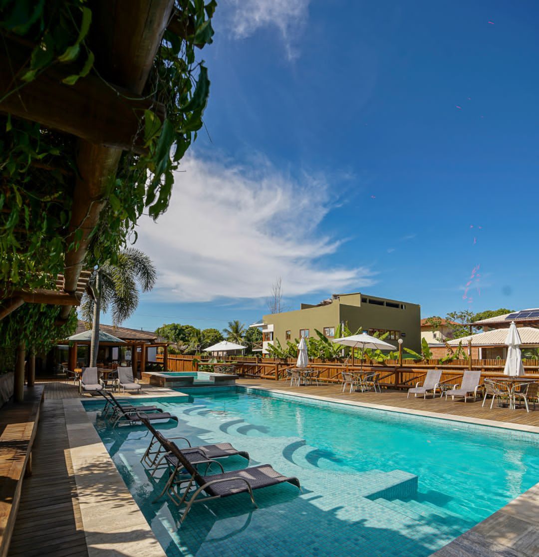 A pool area with lounge chairs and umbrellas, surrounded by wooden deck and greenery.