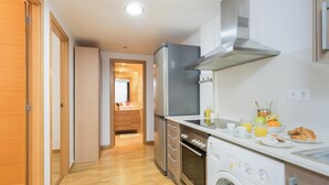Una cocina moderna con piso de madera, horno empotrado, lavadora y refrigerador de acero inoxidable.