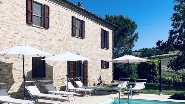 A poolside area with lounge chairs and umbrellas, a stone building with windows, and a clear blue sky. - Villa Bella Rosa (Fratte Rosa)
