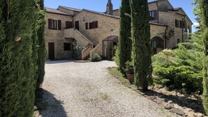 A stone building with a gravel driveway, surrounded by tall cypress trees. - Villa Bella Rosa (Fratte Rosa)