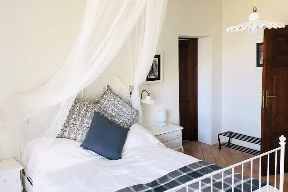 Une chambre à coucher avec un lit sous un dais, des tables de chevet, une commode, une lampe et une porte.