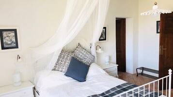A bedroom with a bed under a canopy, bedside tables, a nightstand, a lamp, and a door.