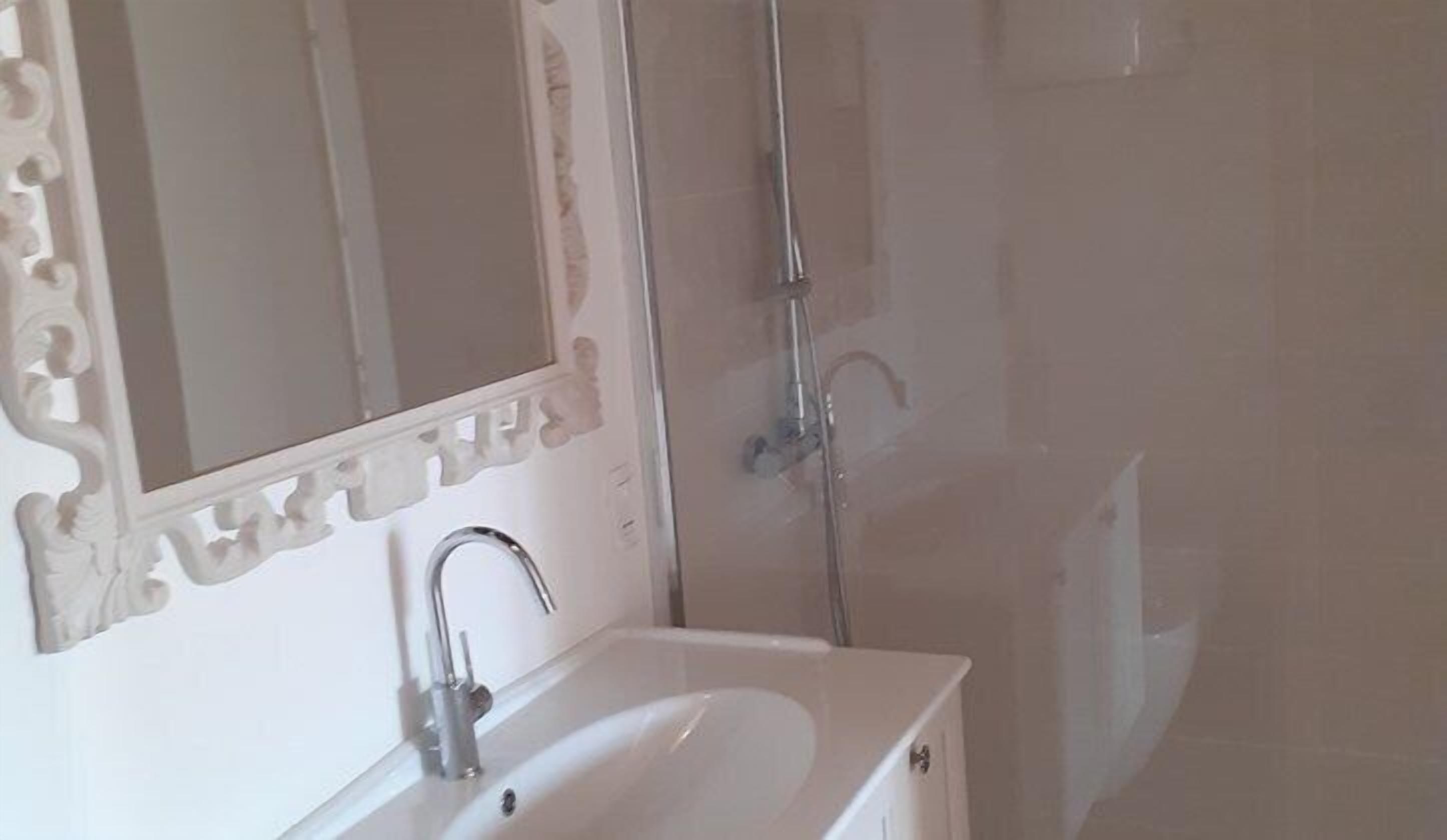 A bathroom with a white sink, a mirror with an ornate frame, and a shower area.