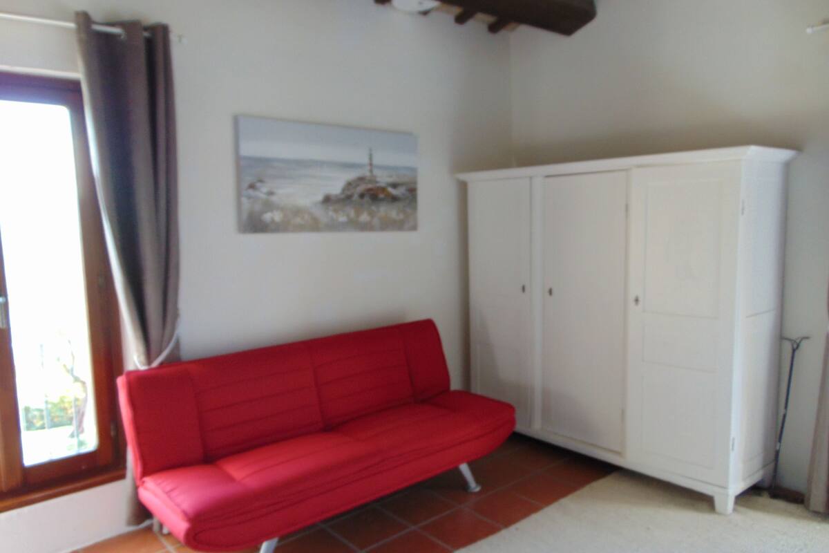 Une pièce avec un canapé rouge, une armoire blanche et un tableau accroché au mur.
