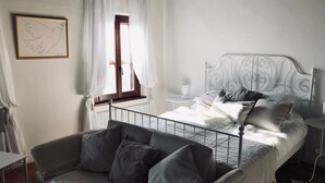 A bedroom with a metal bed frame, a grey sofa, and a white wall with a framed picture. - Villa Bella Rosa (Fratte Rosa)