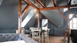 Un espacio tipo loft con vigas de madera a la vista, una zona de comedor con una mesa redonda y sillas, y un amplio ventanal que proporciona luz natural.