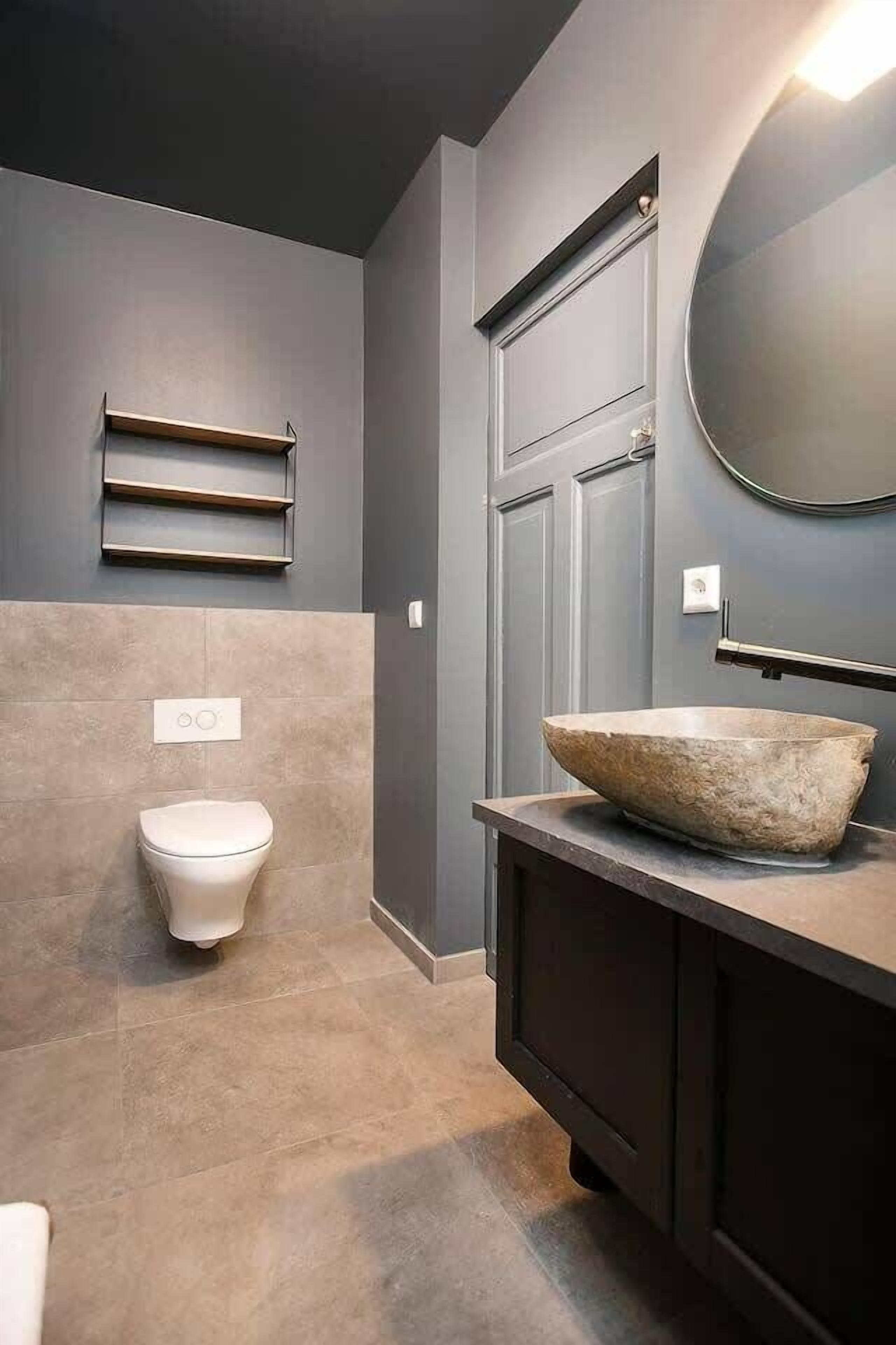 Une salle de bain moderne avec un lavabo en pierre, des toilettes et une étagère fixée au mur.