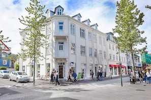 A multi-story building with a white facade, balconies, and a ground-level entrance.