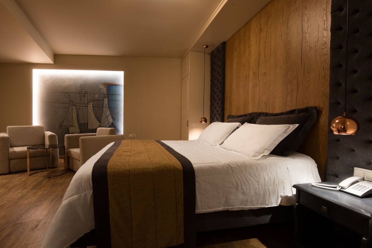 A modern hotel room with a large bed, a desk with a telephone, and a seating area with chairs.