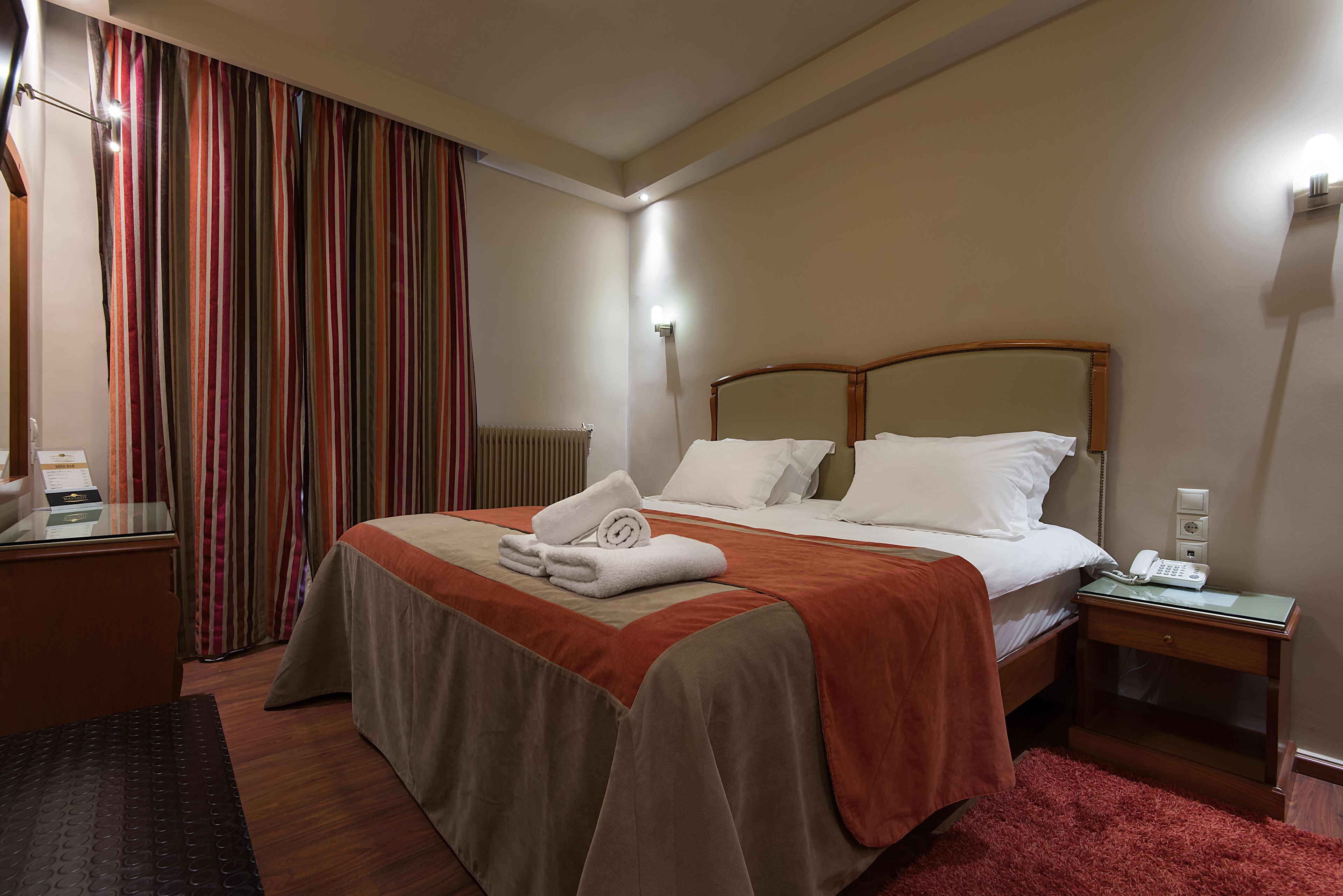 Una habitació d'hotel amb un llit gran, una taula de nit amb un telèfon, una nitzeta i una finestra amb cortines.
