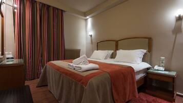 Una habitació d'hotel amb un llit gran, una taula de nit amb un telèfon, una nitzeta i una finestra amb cortines.