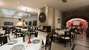 A spacious dining area with multiple tables, chairs, and a central fireplace. - Hotel Kentrikon (Gortynia)