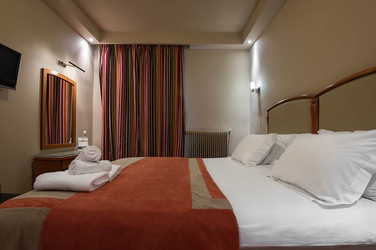 A hotel room with a bed, a nightstand, a mirror, and a window with striped curtains.
