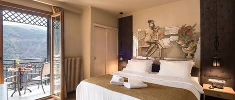 A hotel room with a large bed, a balcony with a table and chairs, and a painting on the wall.