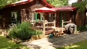 Een rustieke houten chalet met een rood dak, een veranda met buitenmeubilair en een tuin.