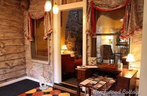 Acogedor interior de una cabaña de troncos con chimenea de piedra, un escritorio de madera con libros y una decoración con forma de gato.