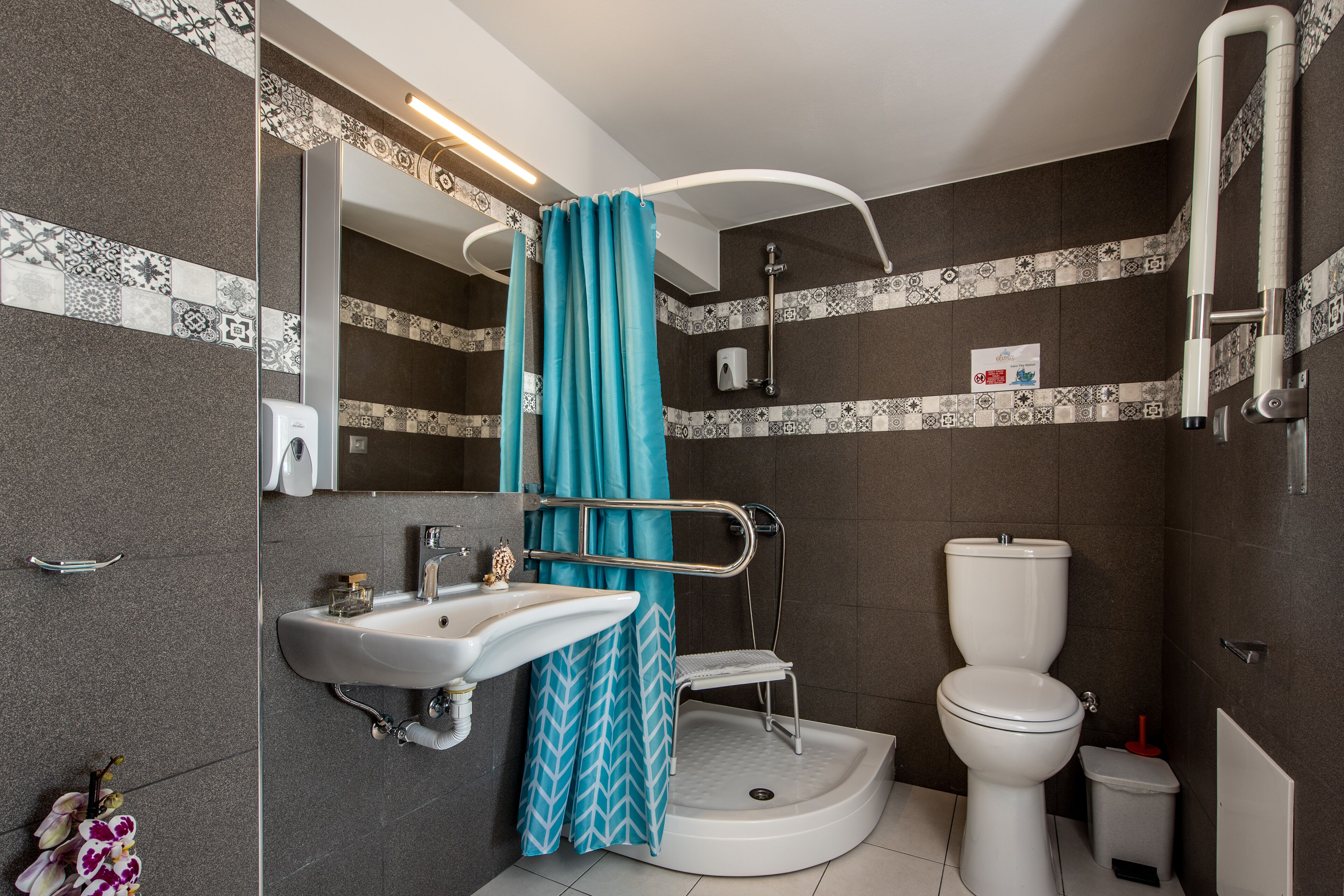 A bathroom with a shower, toilet, sink, and a handrail.
