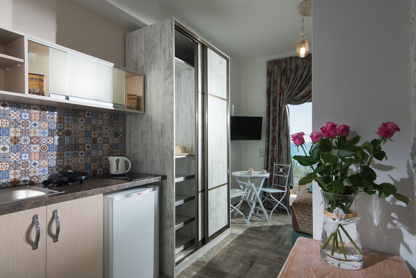 Una cocina compacta con salpicadero de azulejos, un refrigerador pequeño y una zona de comedor con mesa y sillas.