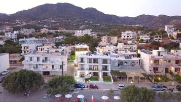 A coastal residential area with modern buildings, a beach with sun loungers, and a mountain backdrop.